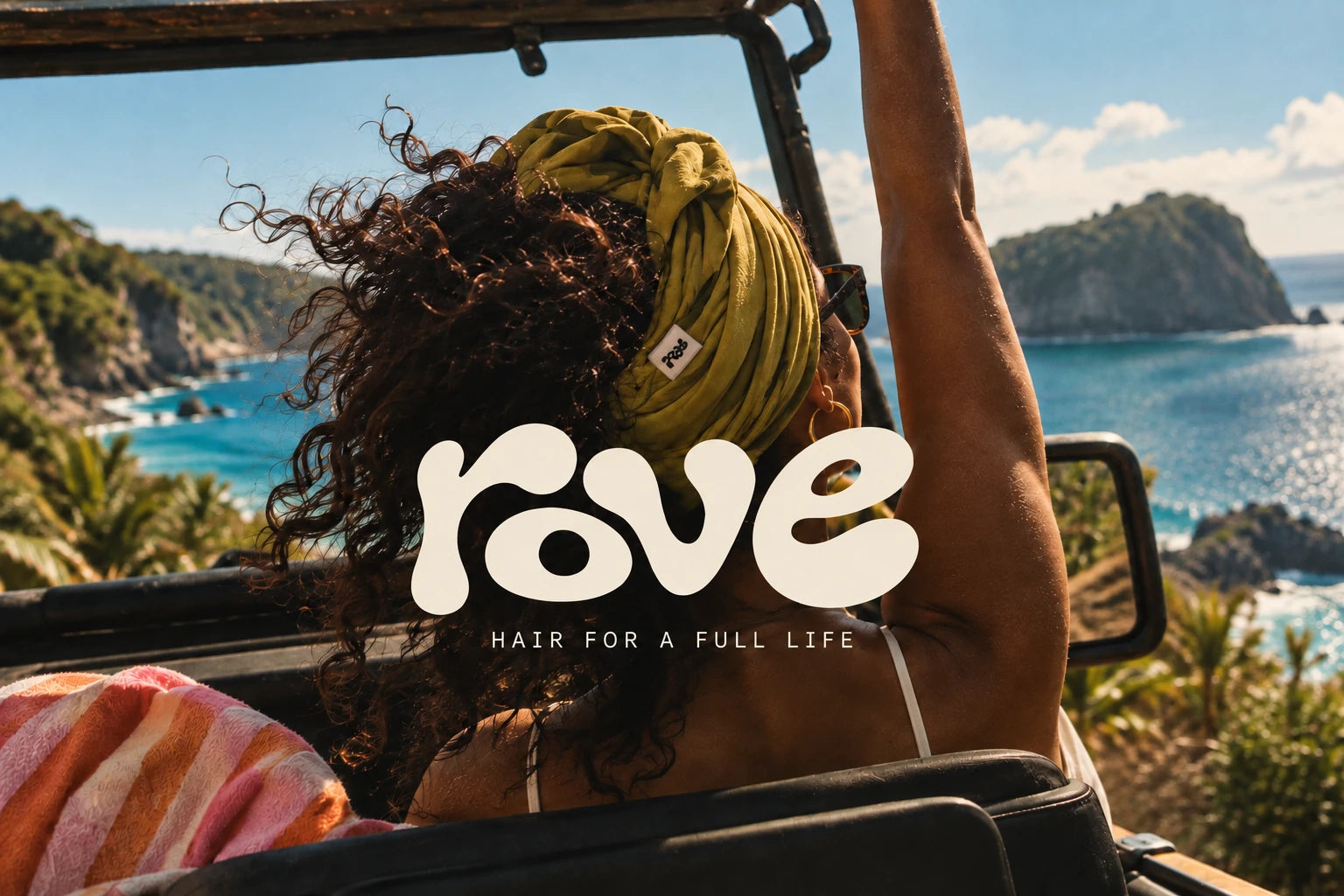 A woman with long, lived-in curls riding in an open-top Jeep above brilliant tropical water